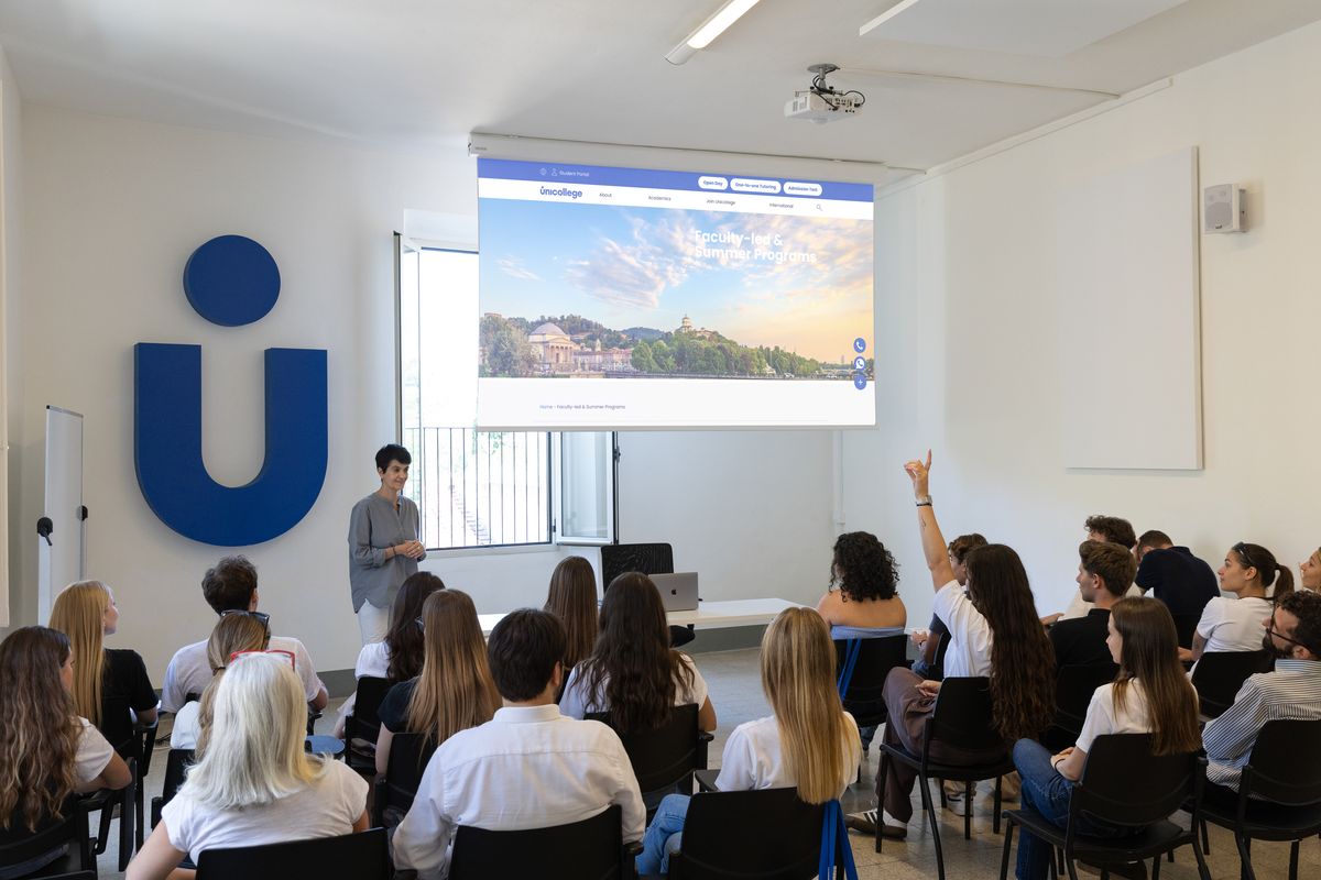 A lecture at Unicollege: students facing the screen and the blue U on the wall
