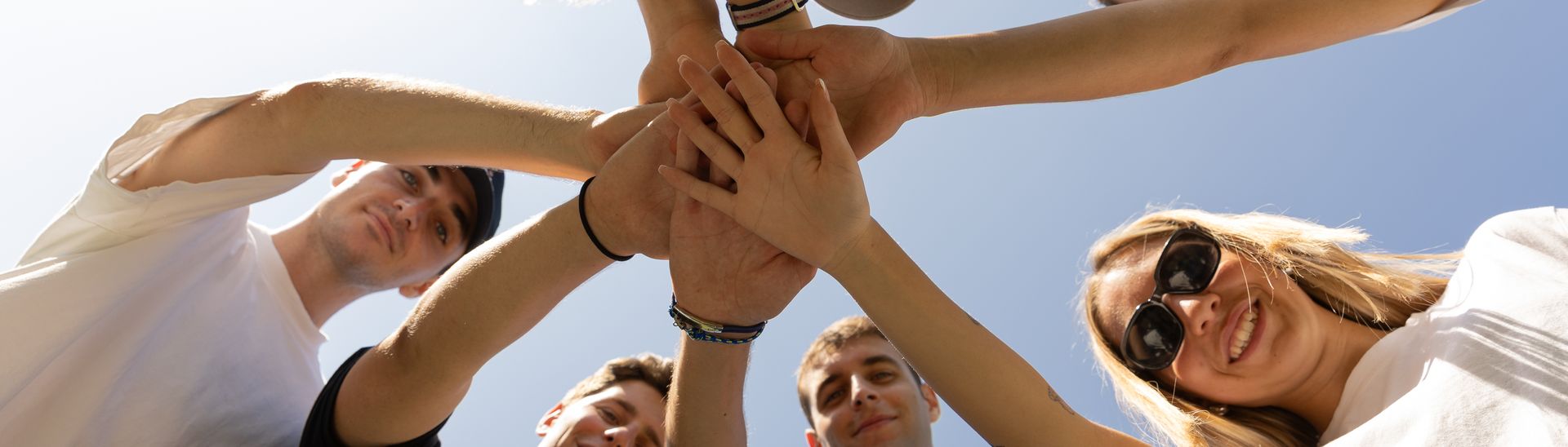 Unicollege students joining hands in a circle, seen from below against the sky