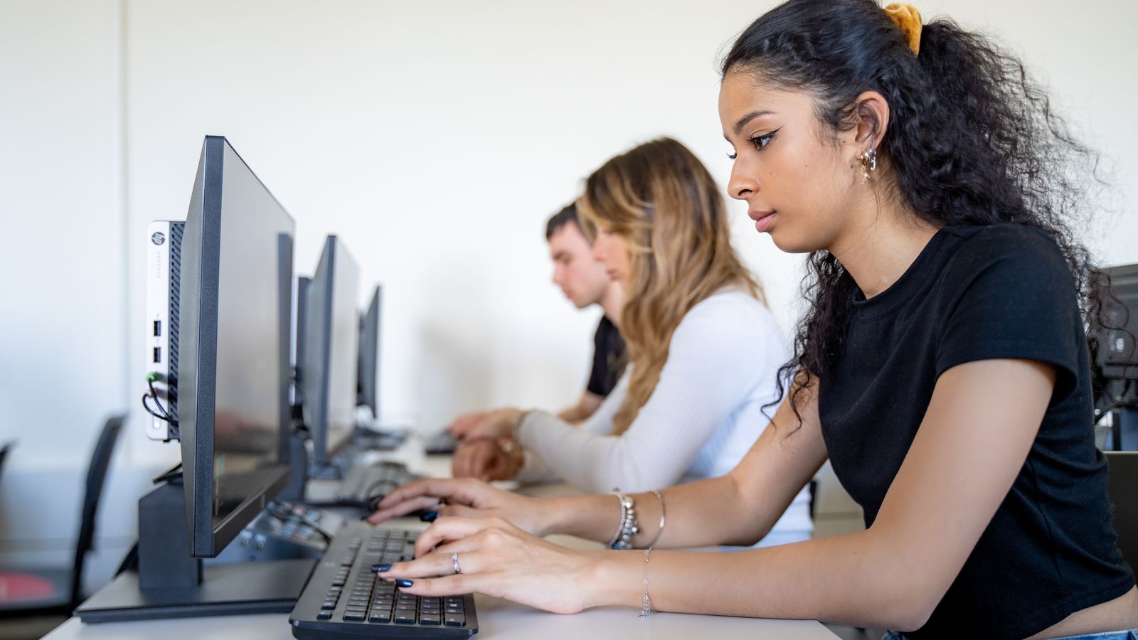 A student typing at a workstation in the Unicollege computer lab