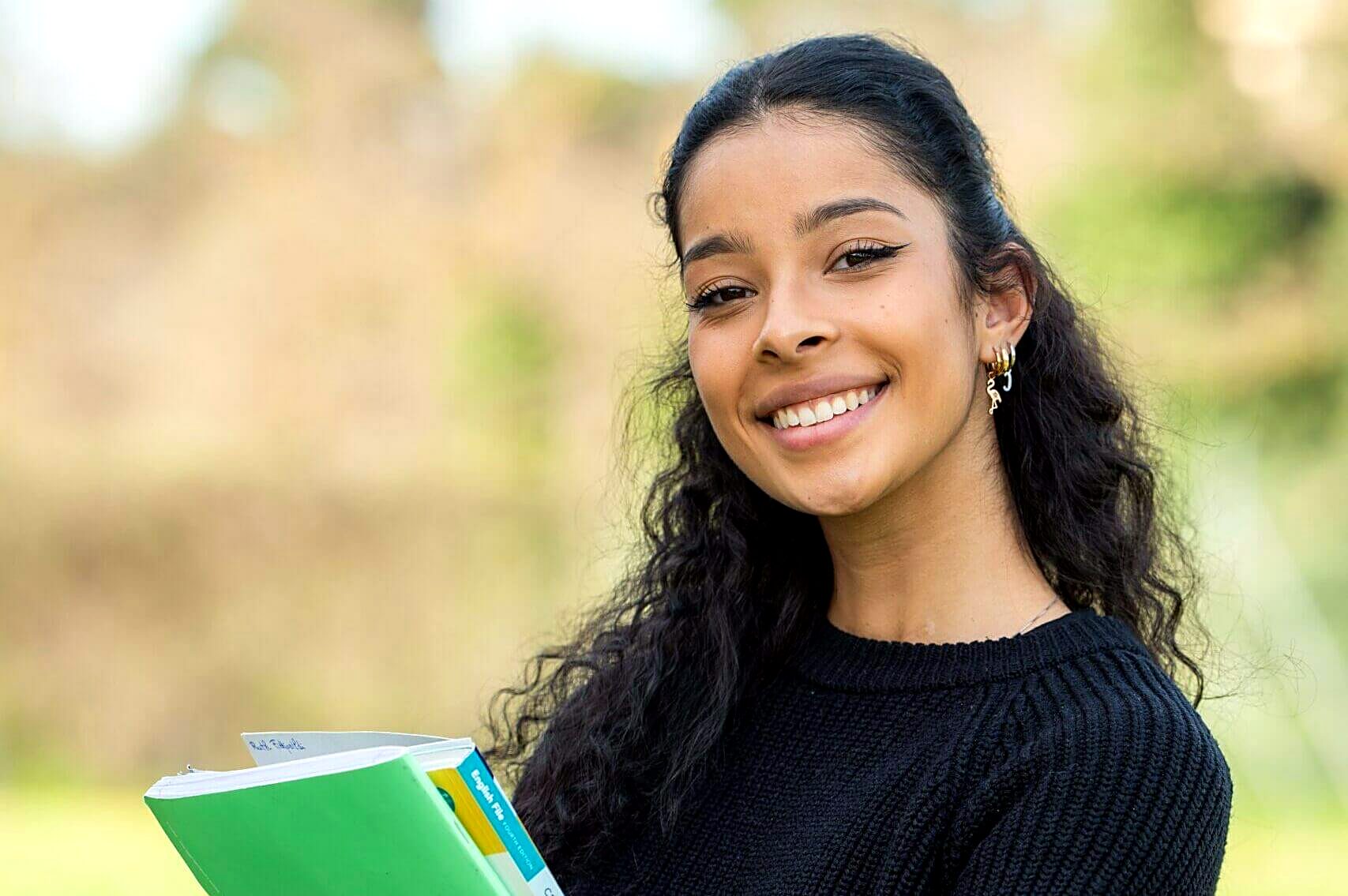 Smiling student holding her notebooks outdoors on campus