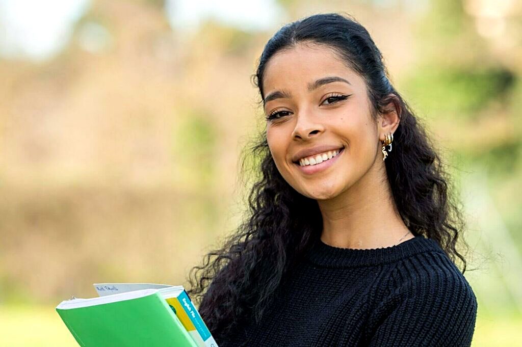 Smiling student holding her notebooks on campus